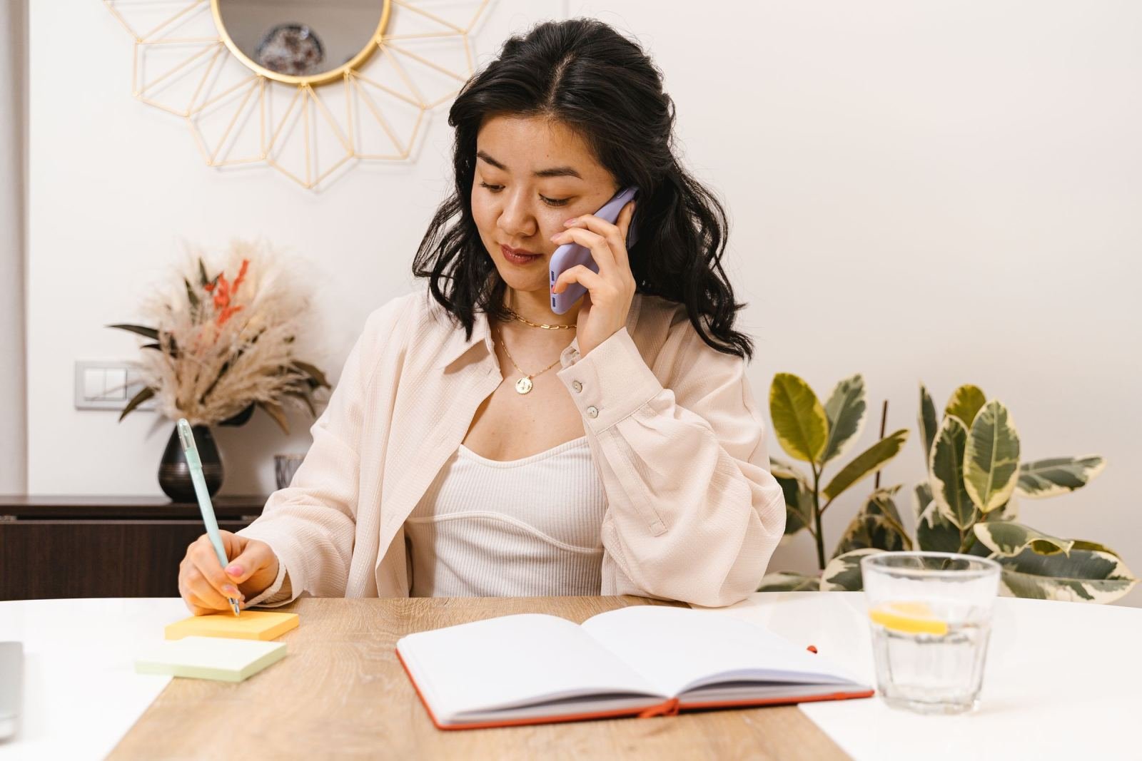 A woman talks on a smartphone while writing notes at a table