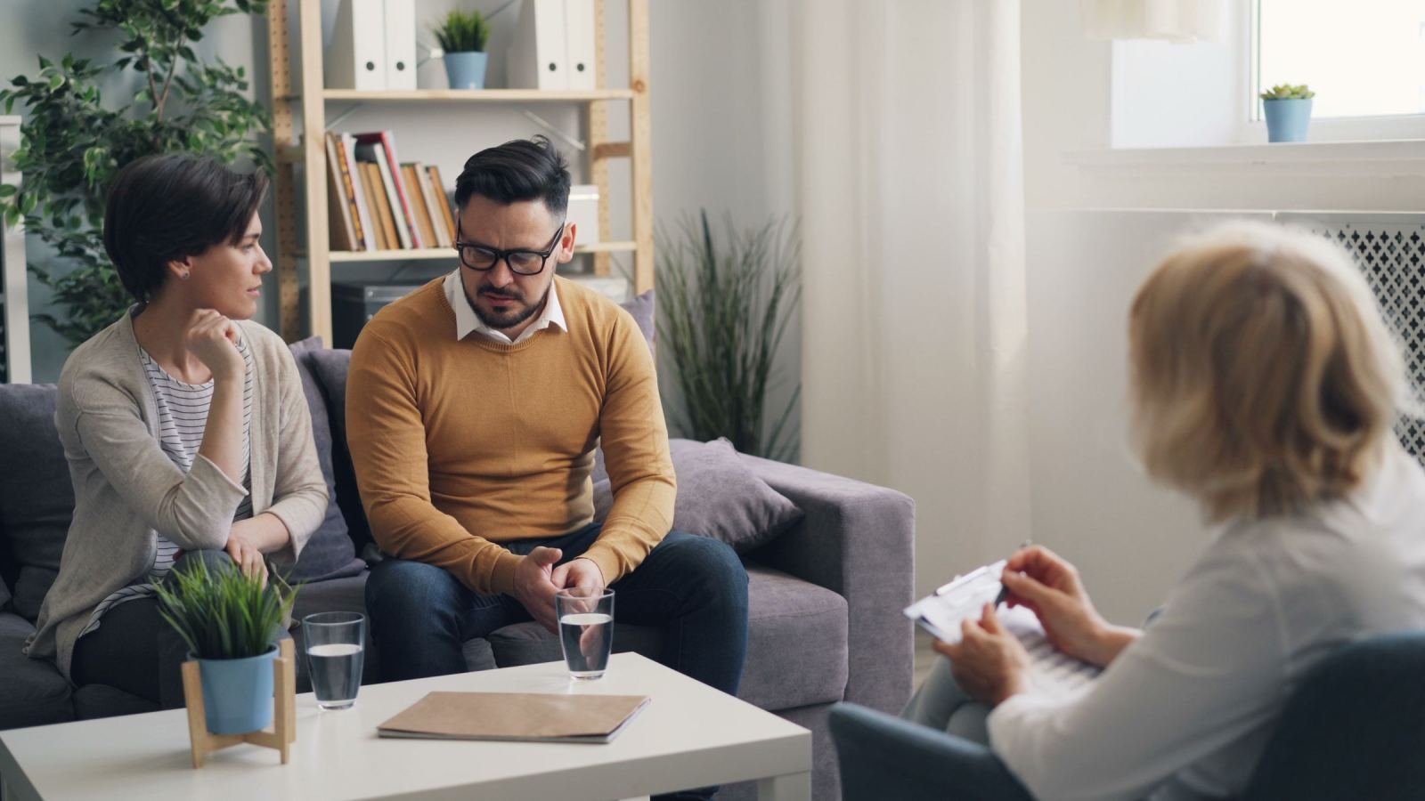 Two people sit on a couch speaking with a pro who holds a pad.