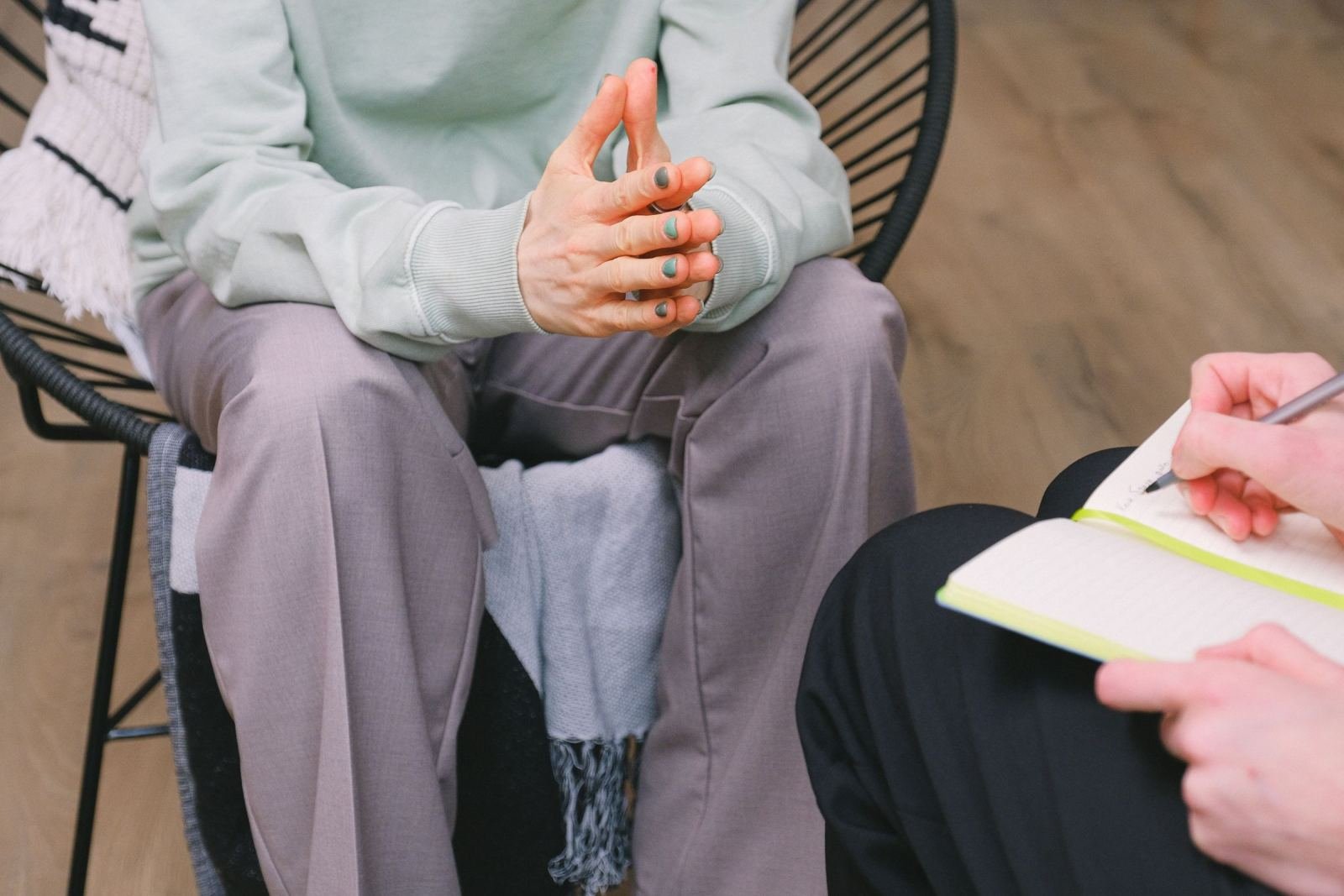 A person gesturing with their hands while another person takes notes in a notebook
