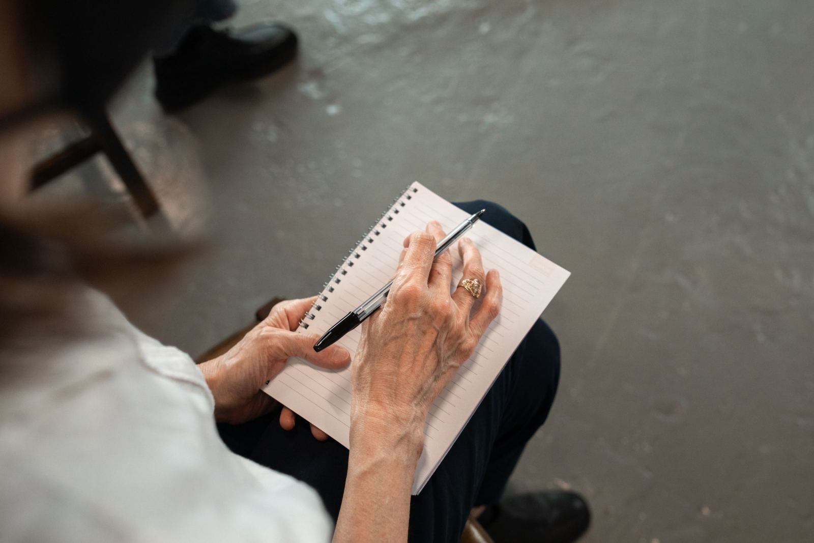 A person's hands writing in a spiral notebook with a black pen