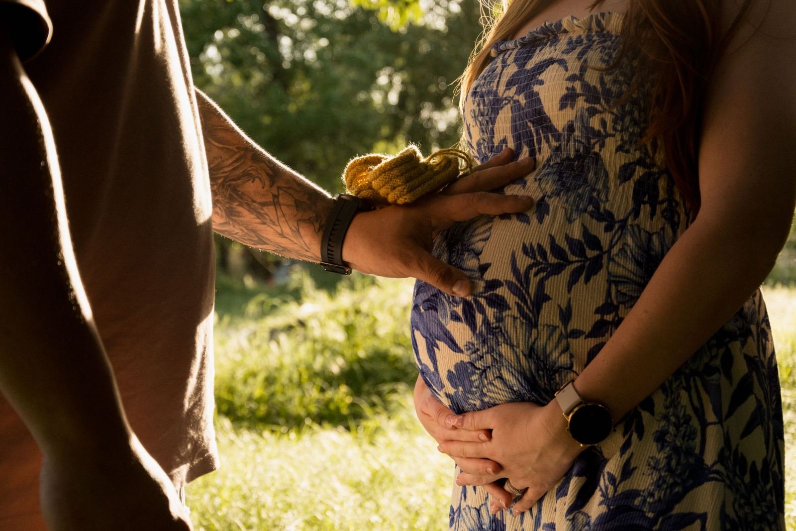 A man and a pregnant woman place their hands on her belly with a small yellow baby shoe