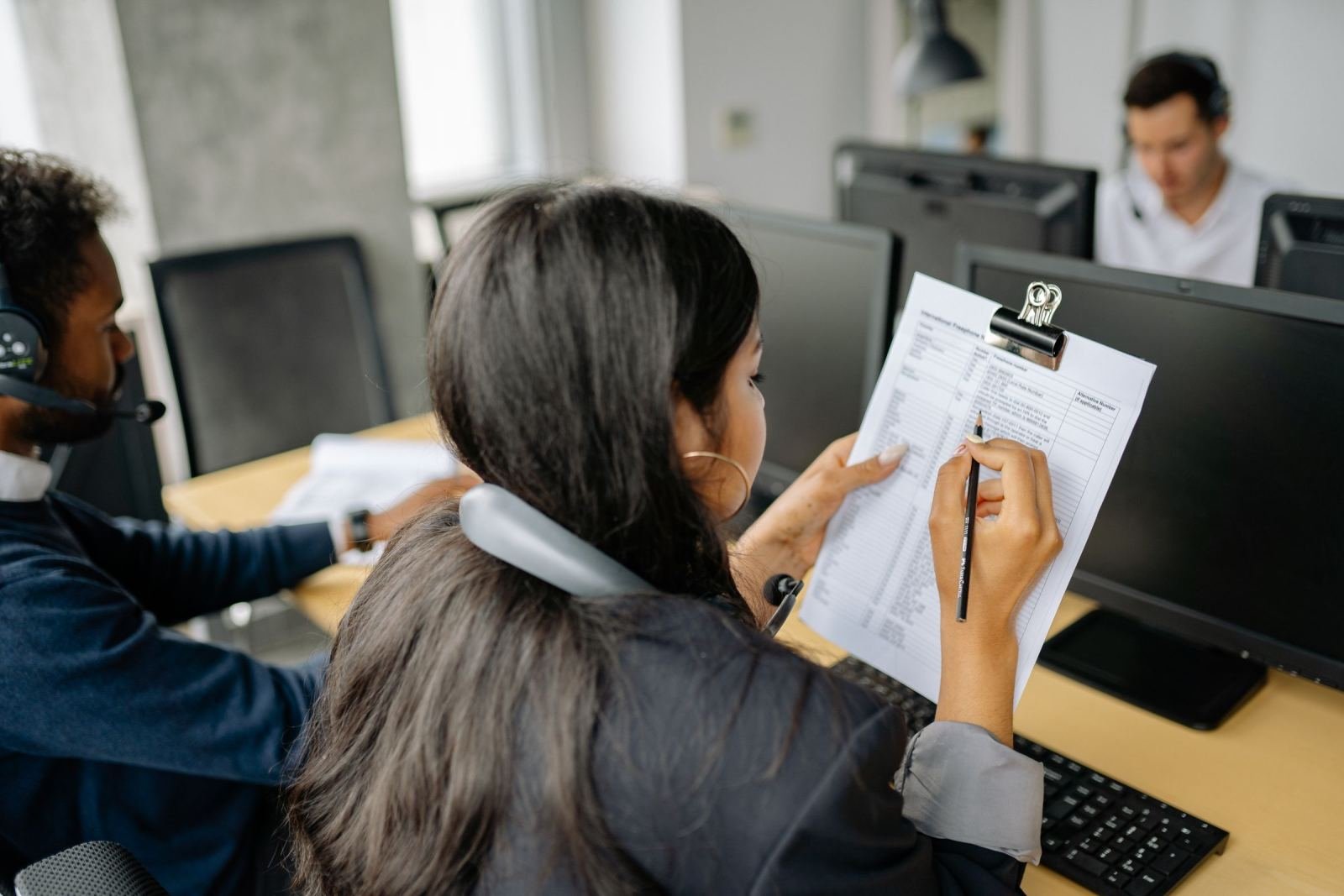 A woman writes on a clipboard while sitting at a desk in a bright office