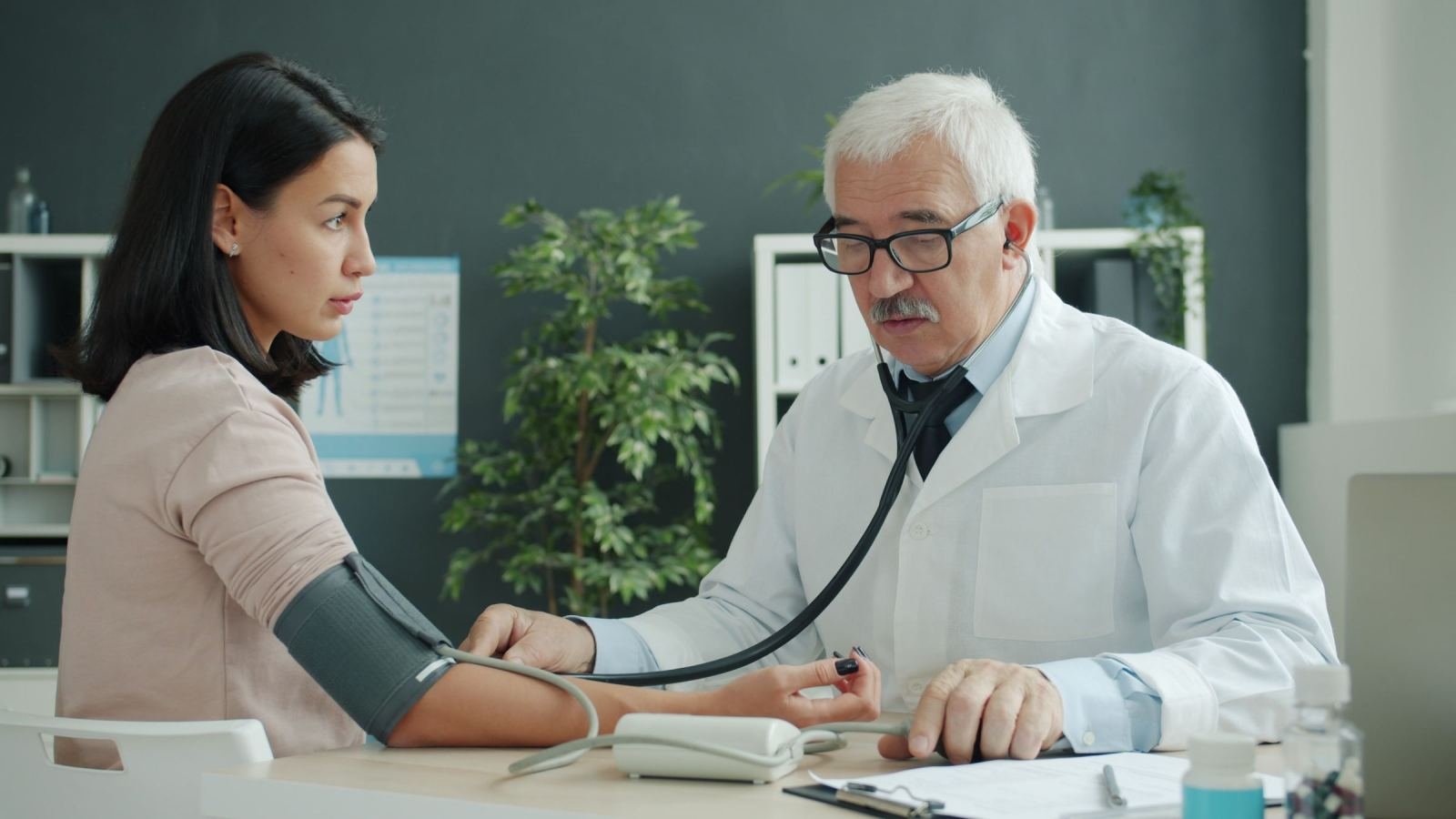 In a well-lit room, a doctor wraps a blood pressure cuff around a patient's arm.