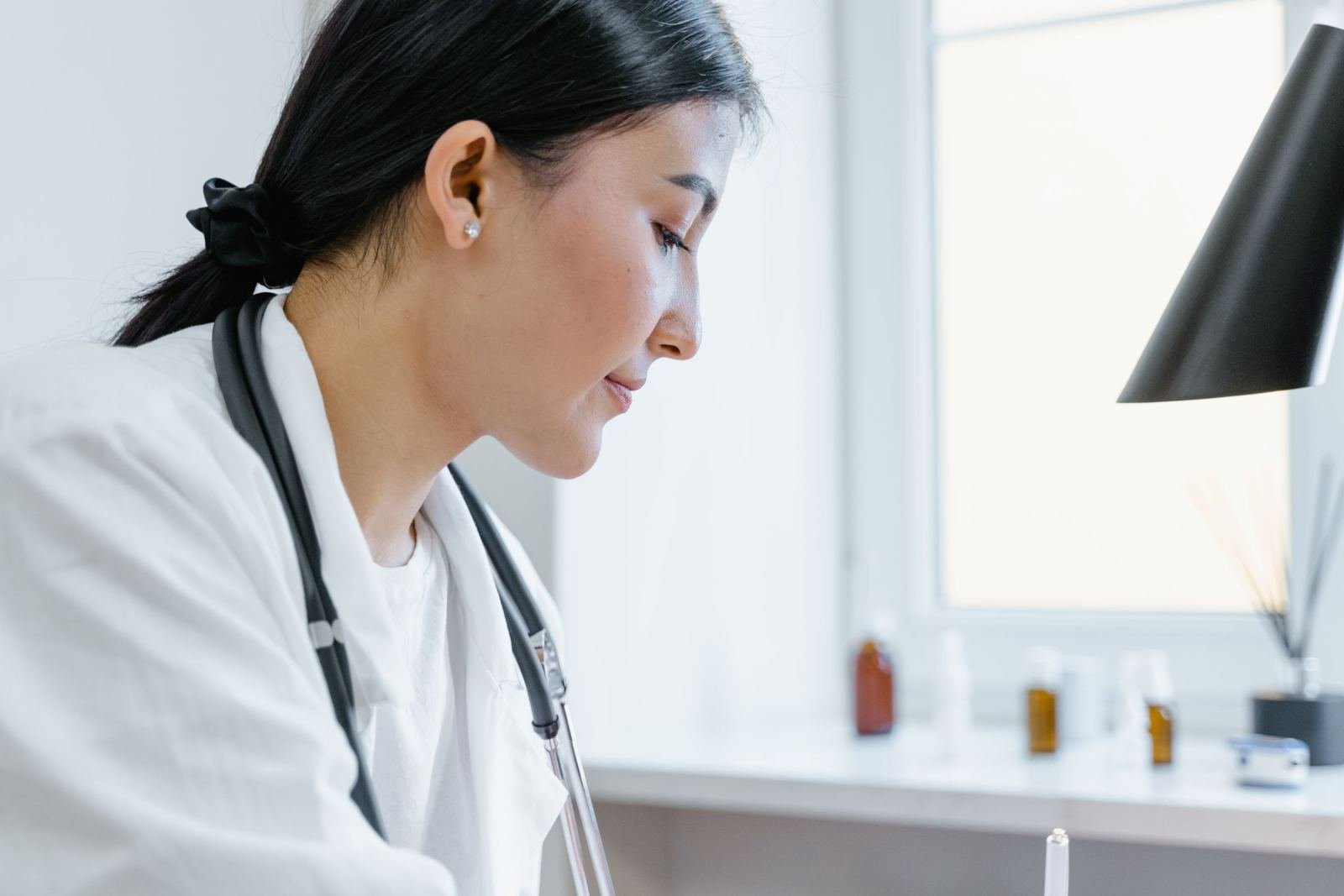 A clinician in a white coat and stethoscope looks down in a medical office