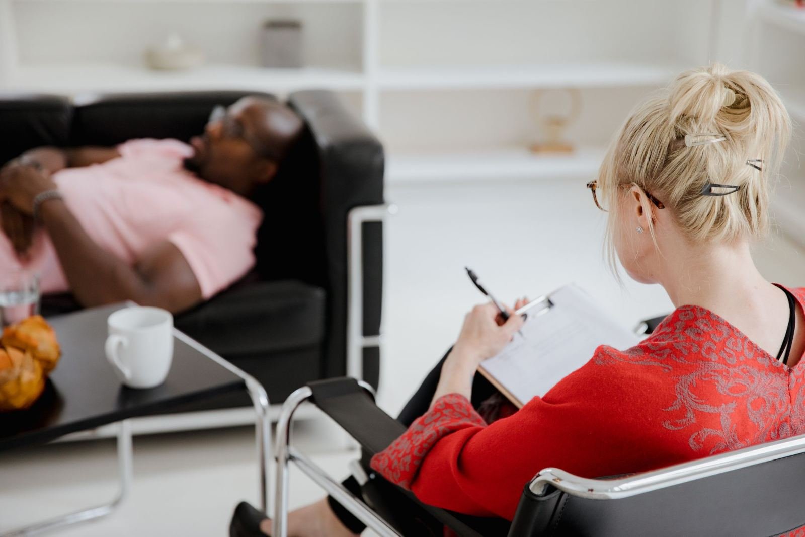 A woman taking notes on a clipboard while talking to a man reclining in a chair