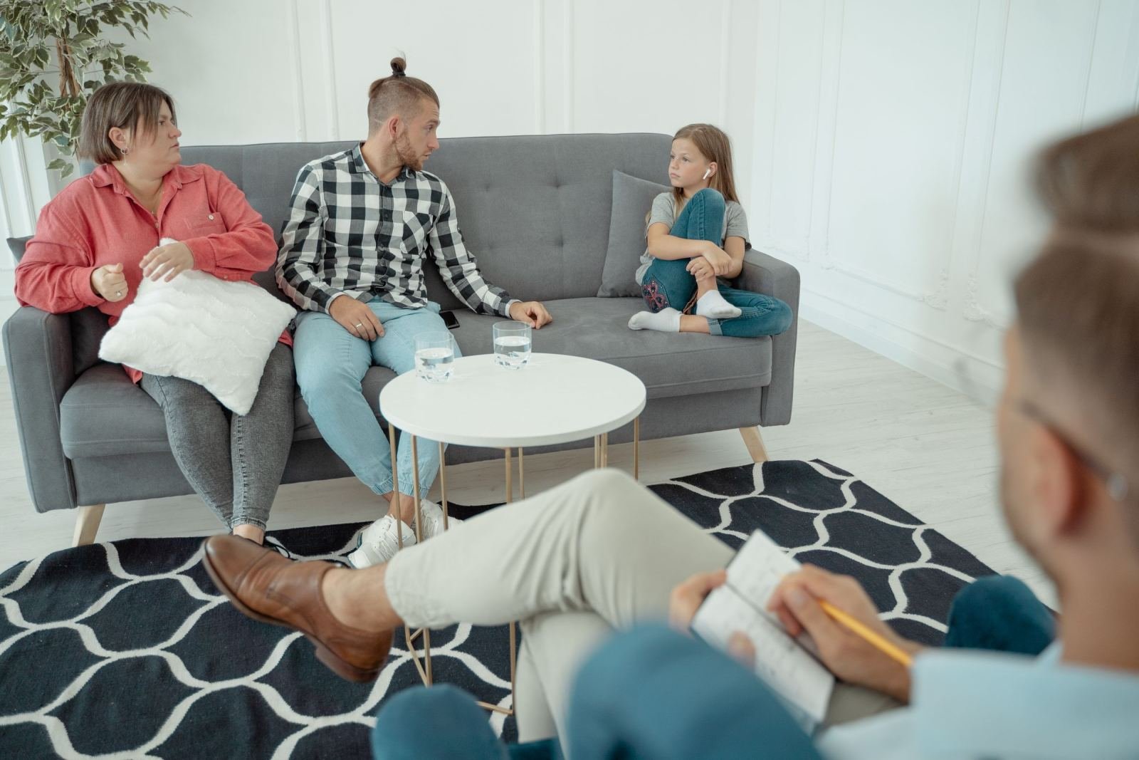 A counselor makes notes while a family of three rests on a couch