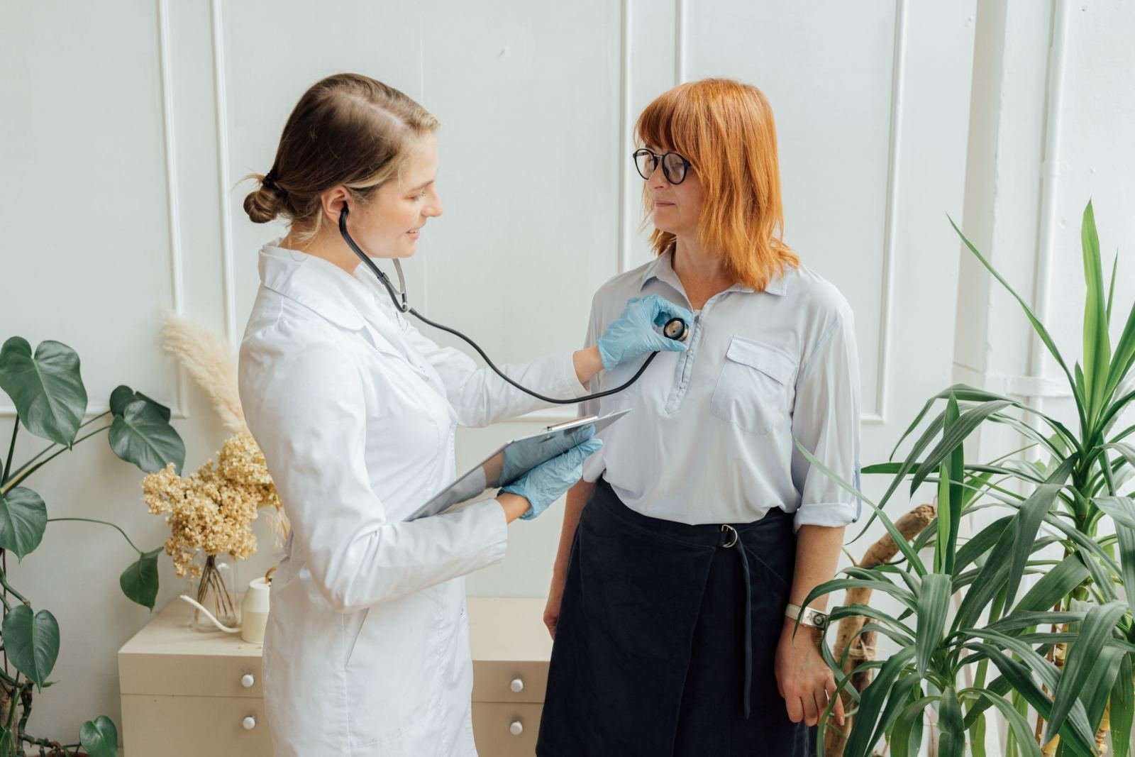A clinician in a white coat uses a stethoscope to examine a patient