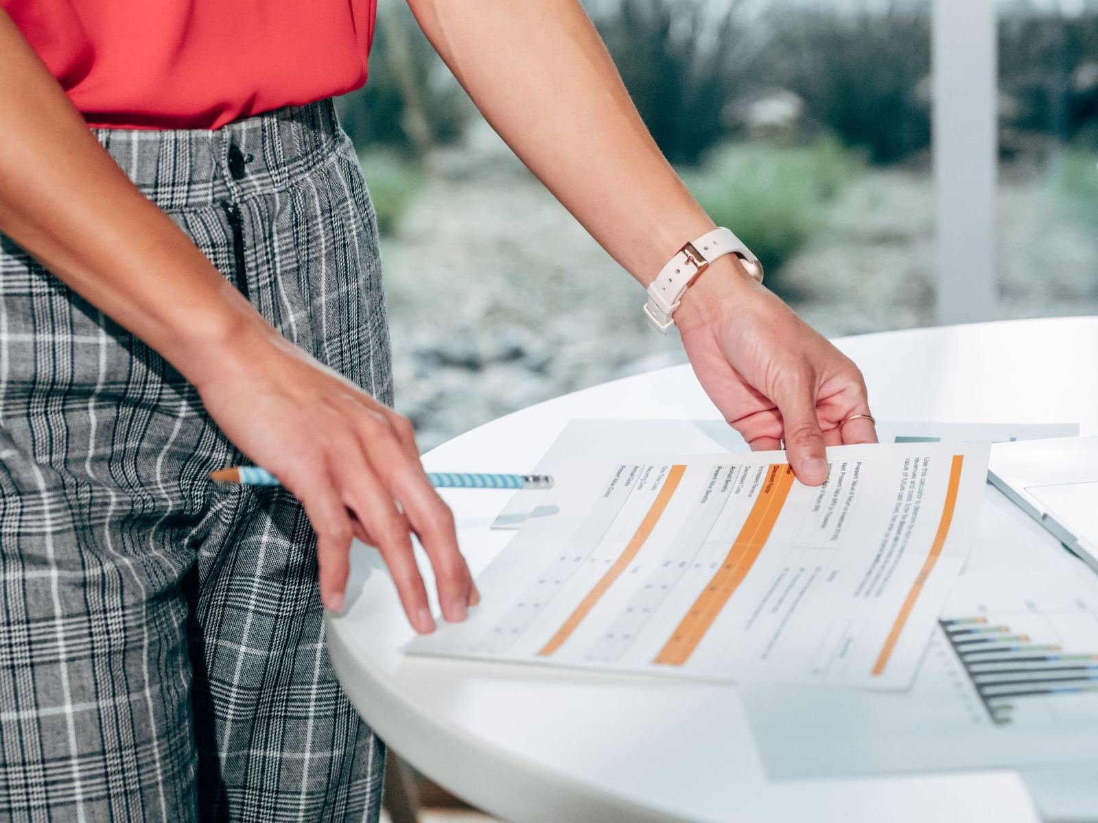 Someone in plaid pants looks at a marked-up paper on a white table