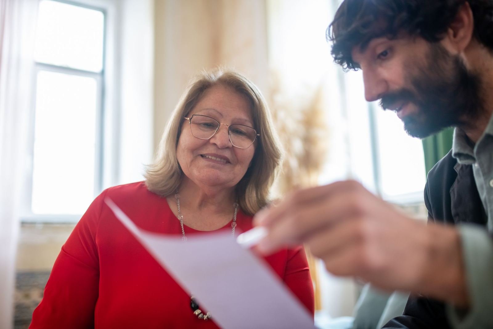 A woman in a red shirt and glasses looks at a man holding a document