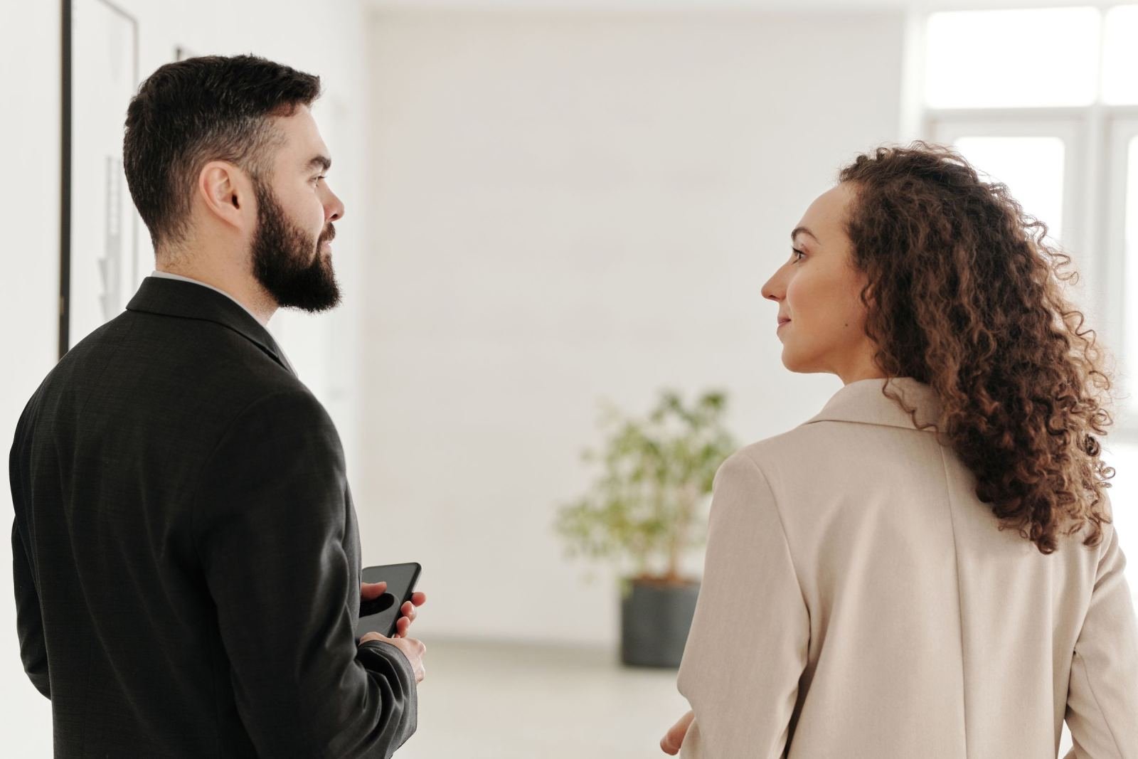 A man and woman in professional attire stand facing each other in a bright room