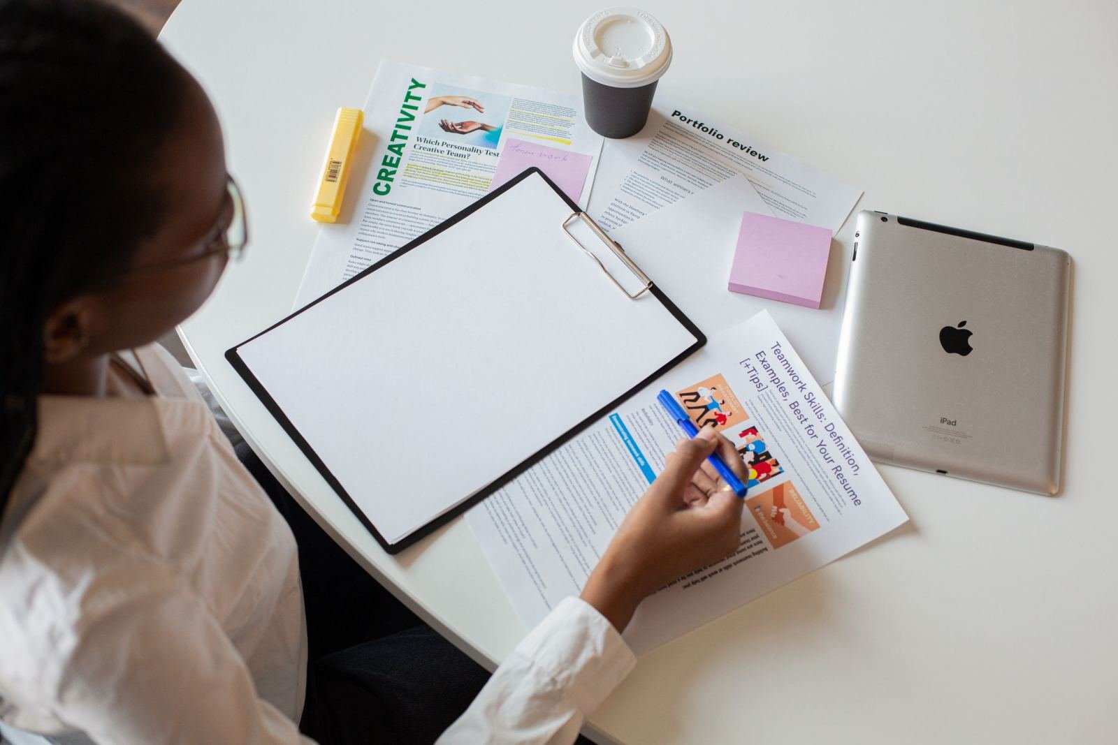 A person holds a pen over documents and a blank clipboard on a white table
