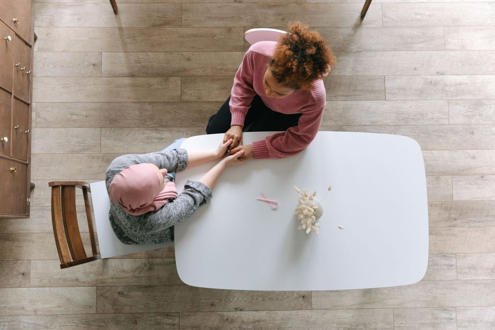 Two women hold hands while sitting across from each other at a white table