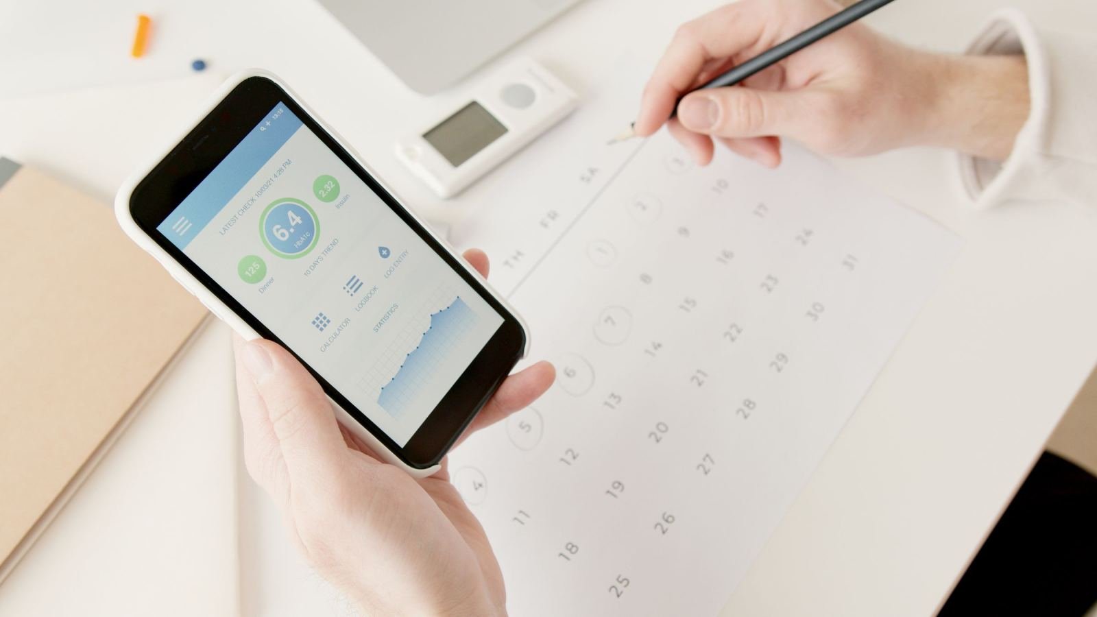 A person uses a health tracking app on a phone near a paper calendar.