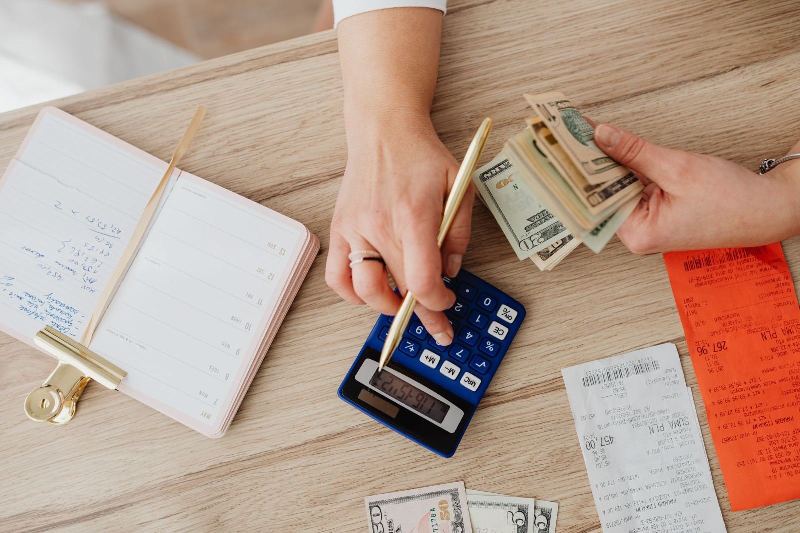 Hands using a calculator and holding cash next to a notebook and receipts