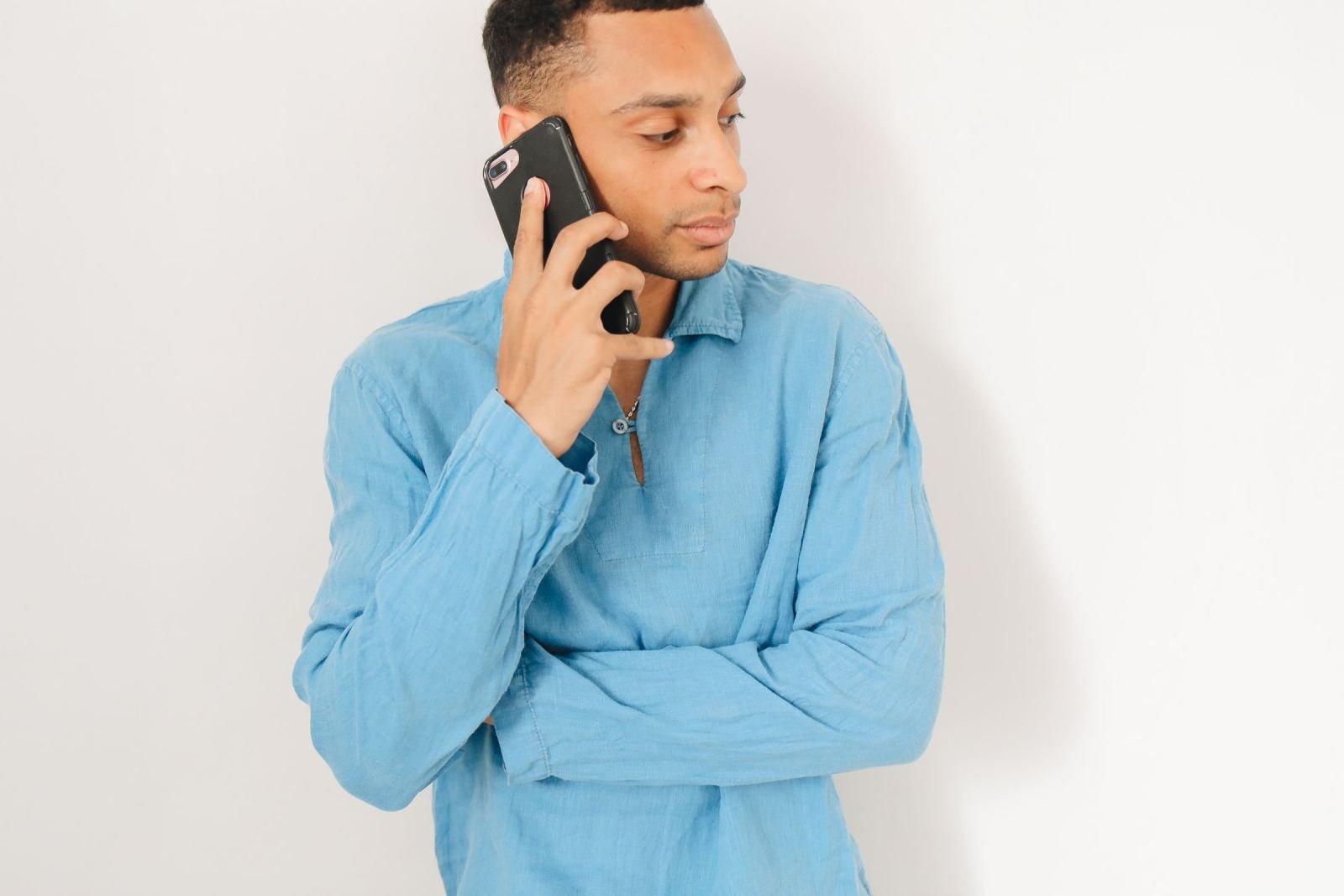 A man in a blue shirt talks on a black smartphone against a white background