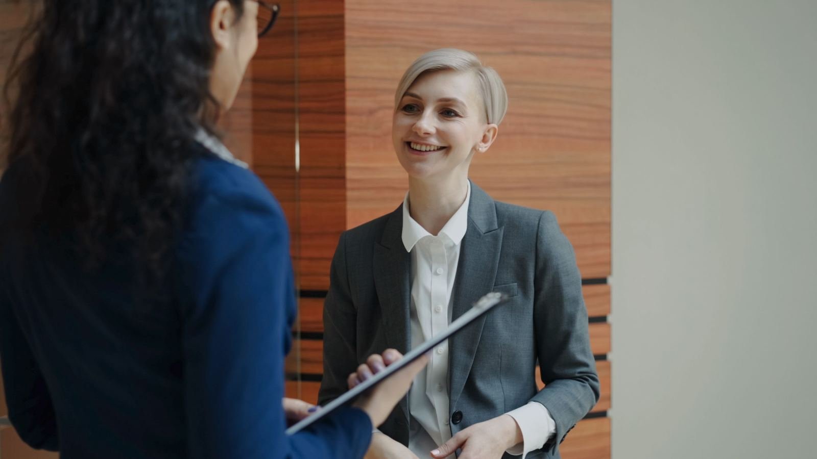 A smiling staff member with a clipboard speaks to a client in a professional setting