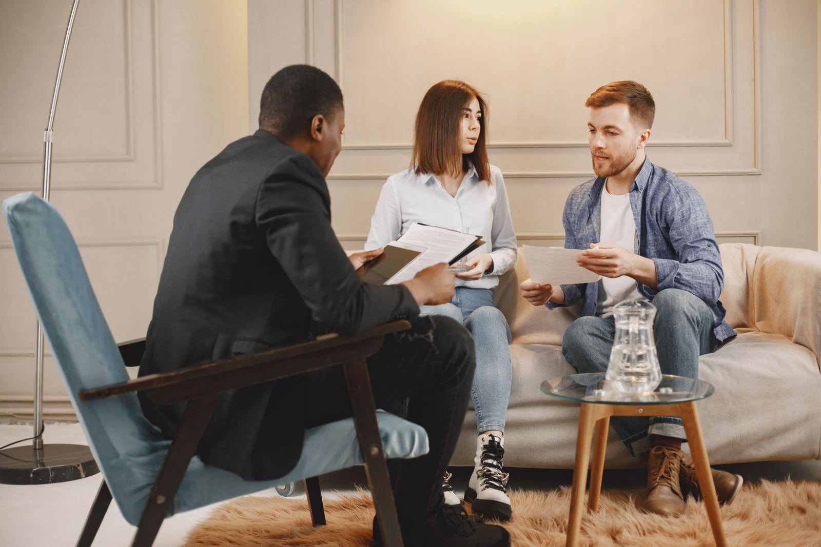 In a modern office, a suited counselor talks with a couple sitting on a sofa.