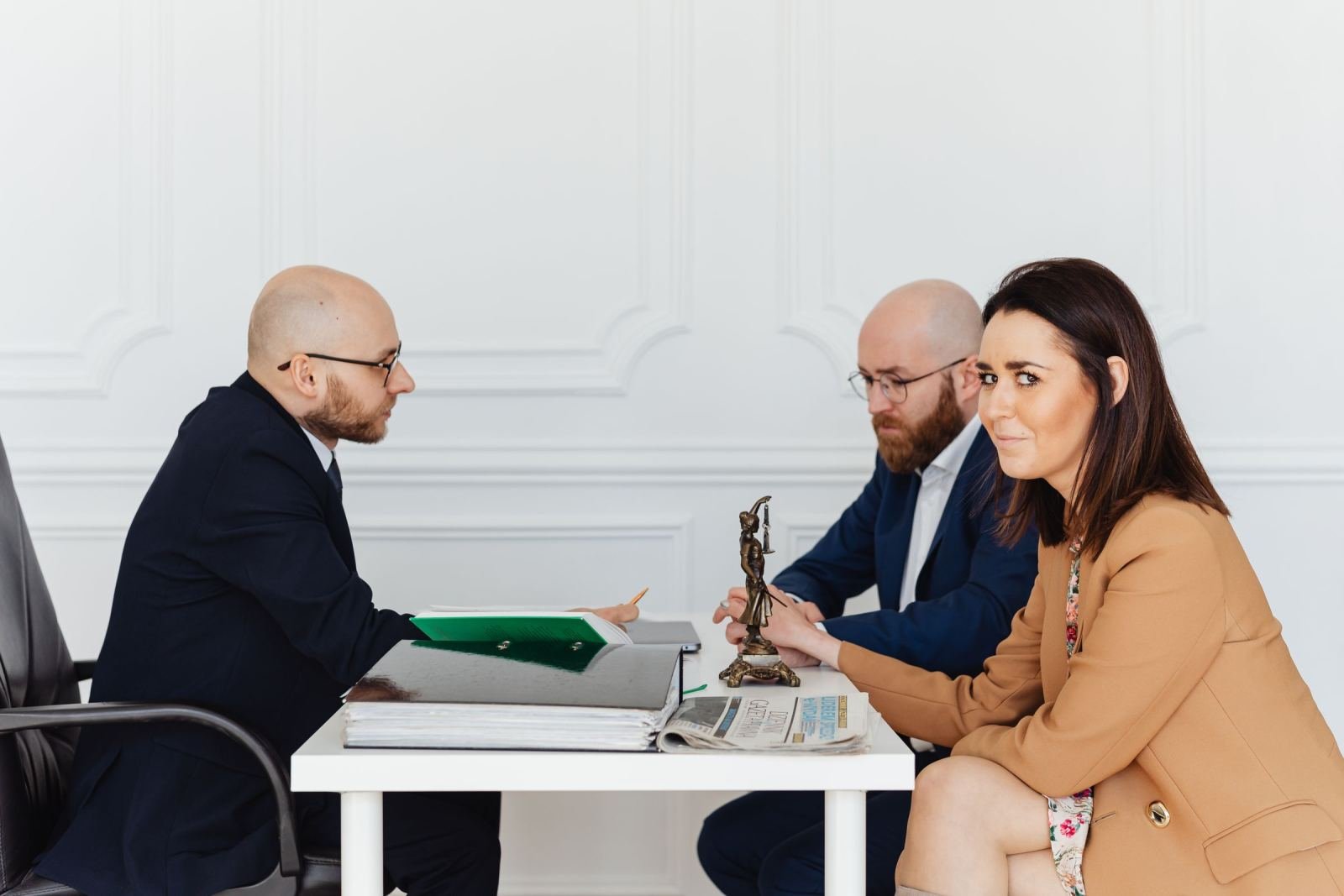 A man in a suit sits at a desk across from a man and a woman in a white office