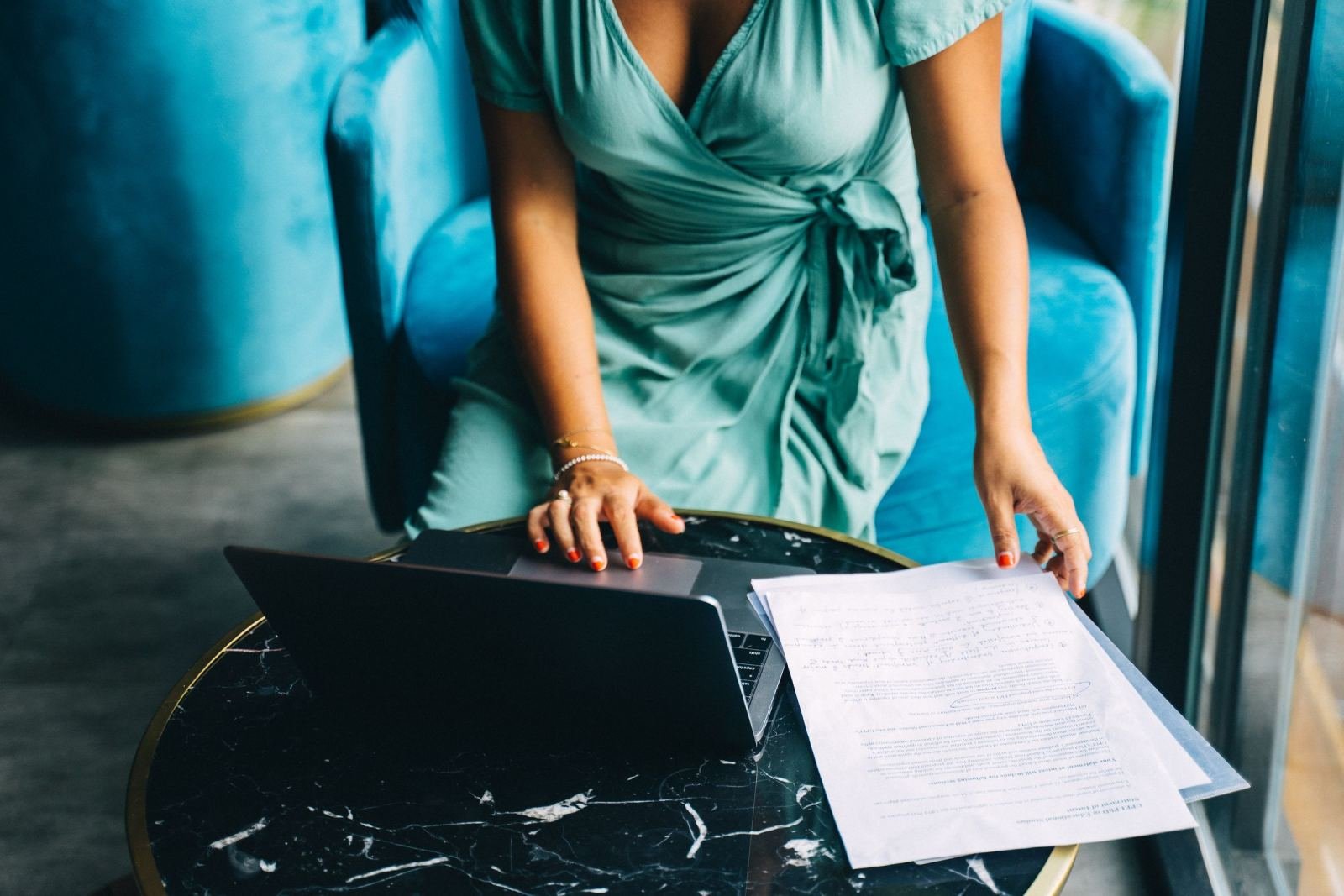 A woman in a blue dress reviews papers next to a laptop on a marble table