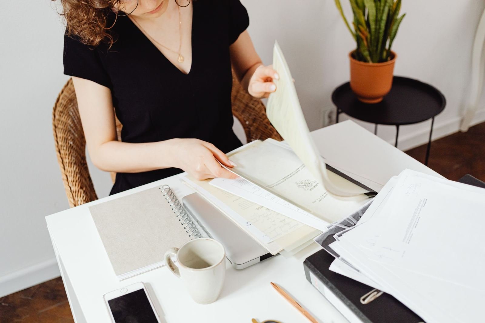 A person sorting through papers and folders at a white desk