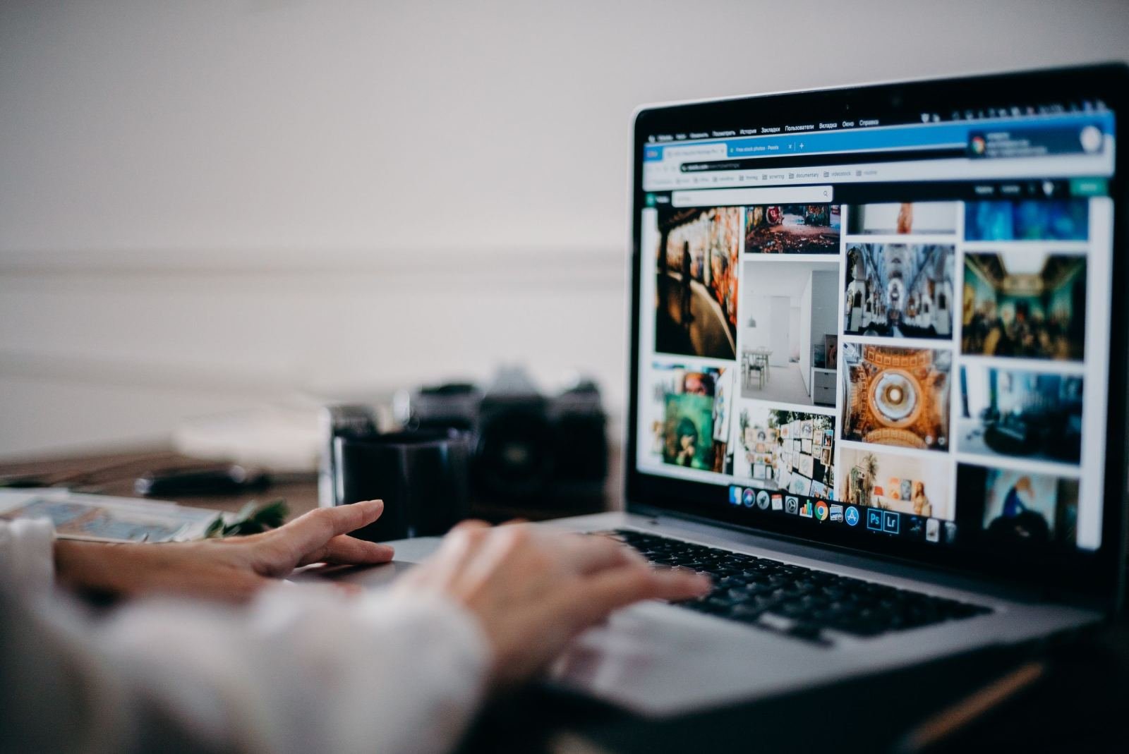Hands typing on a laptop displaying a gallery of images on the screen