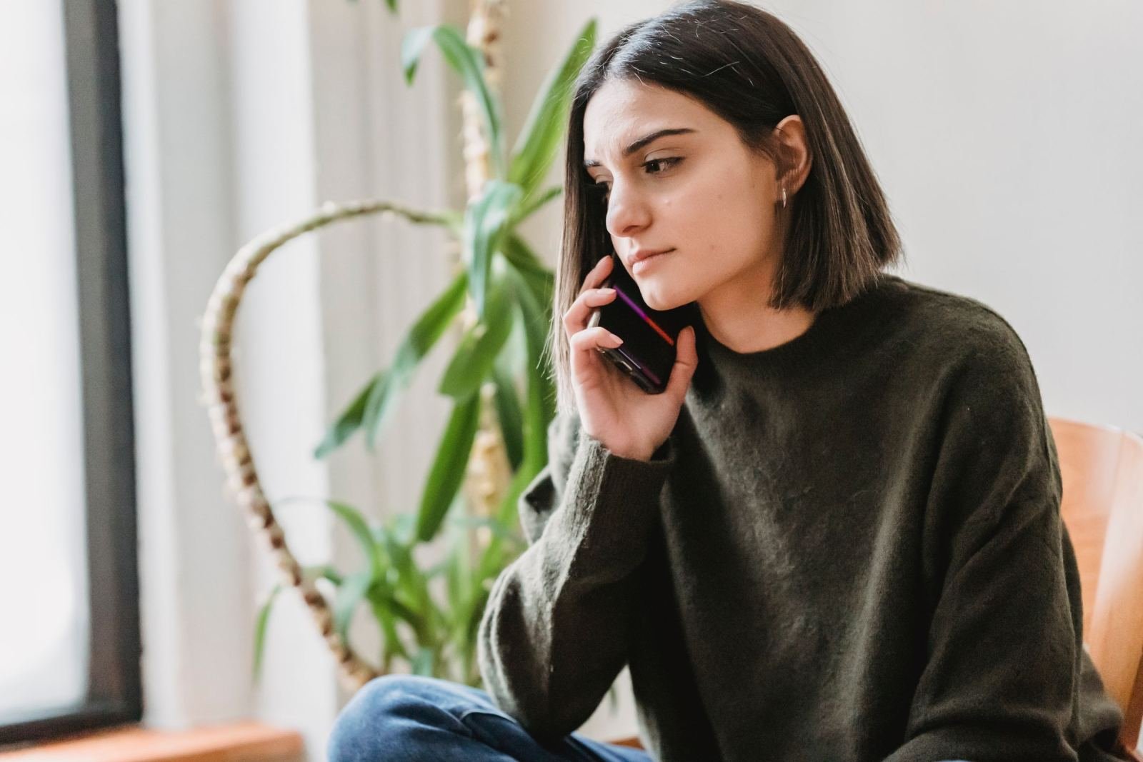 A woman in a green sweater talks on a mobile phone near a window
