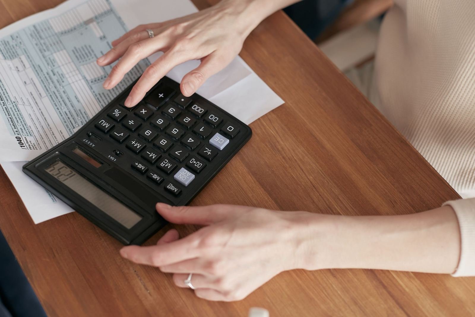 Hands using a calculator next to printed financial documents on a wooden table