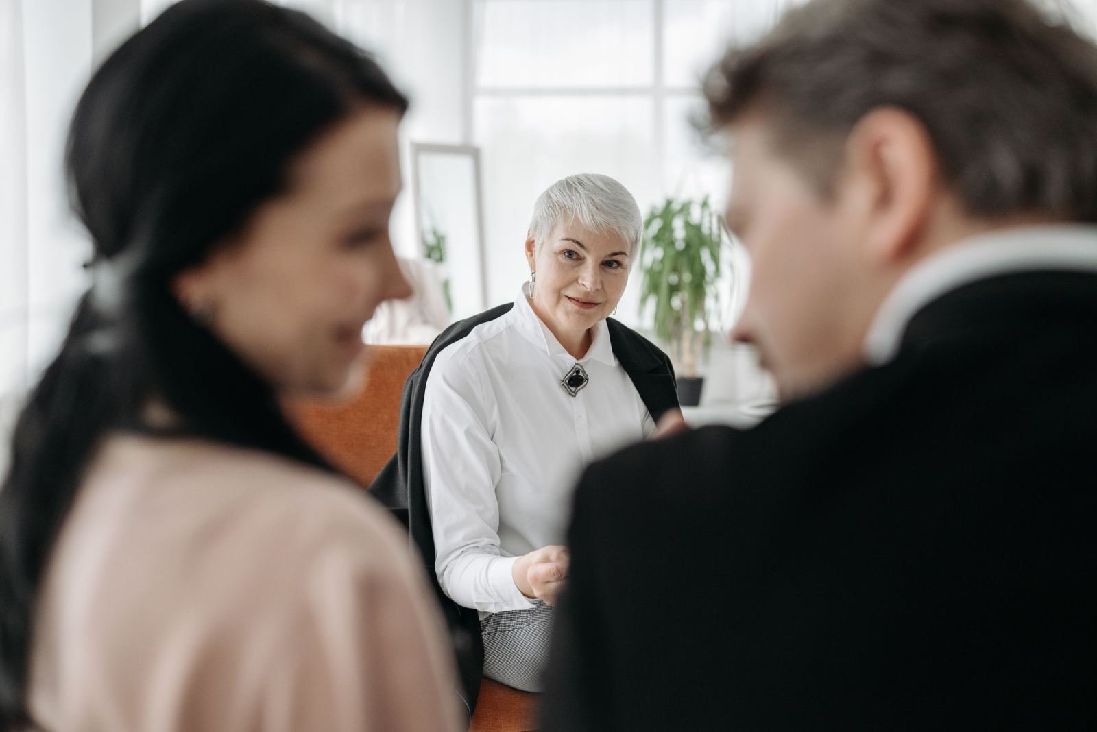 A professional woman in a white shirt talks with a couple in a bright office