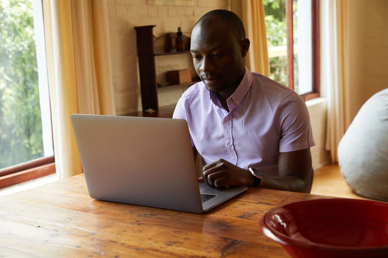 A man in a purple shirt uses a laptop at a wooden table