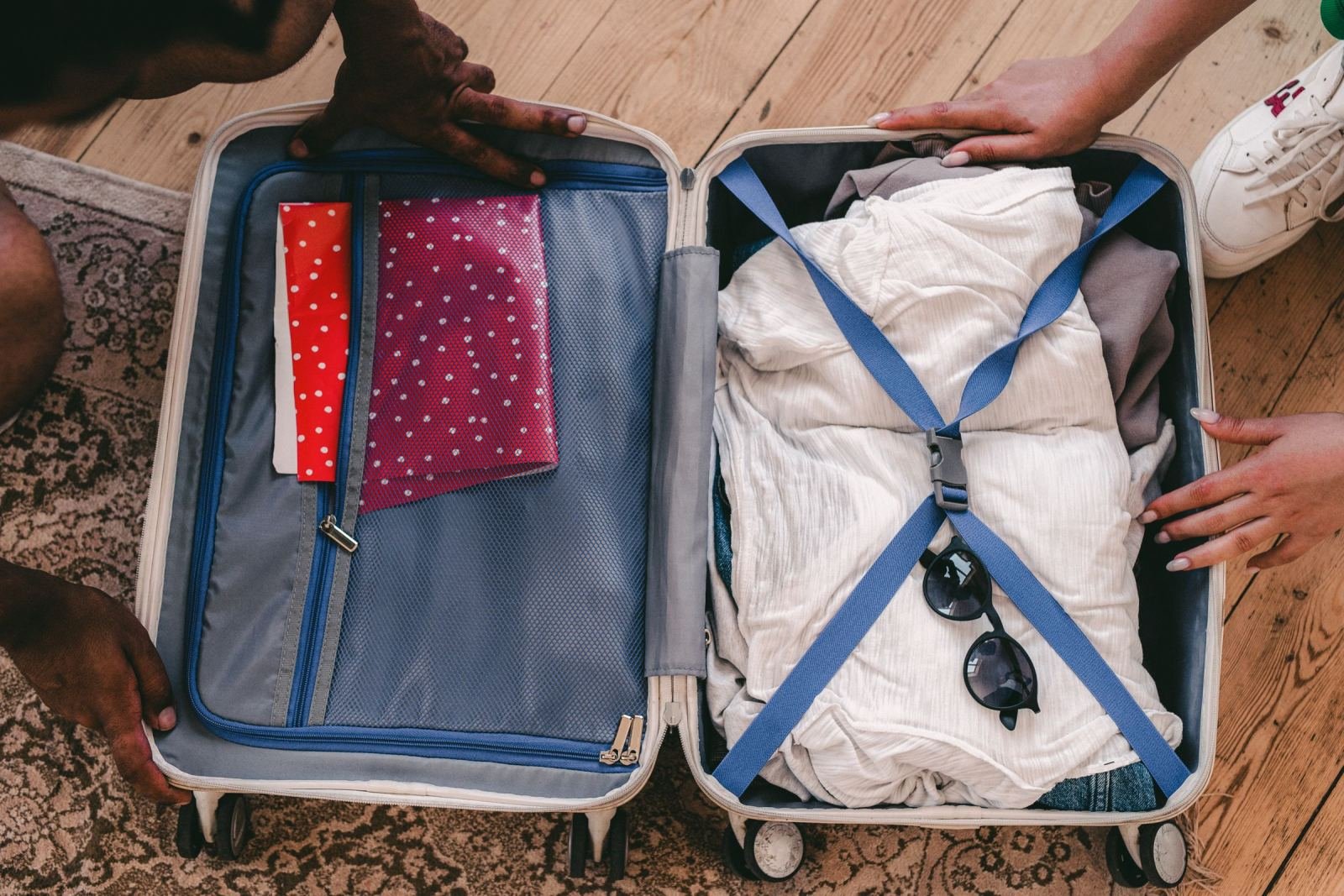 An open suitcase packed with clothes and notebooks on a wooden floor