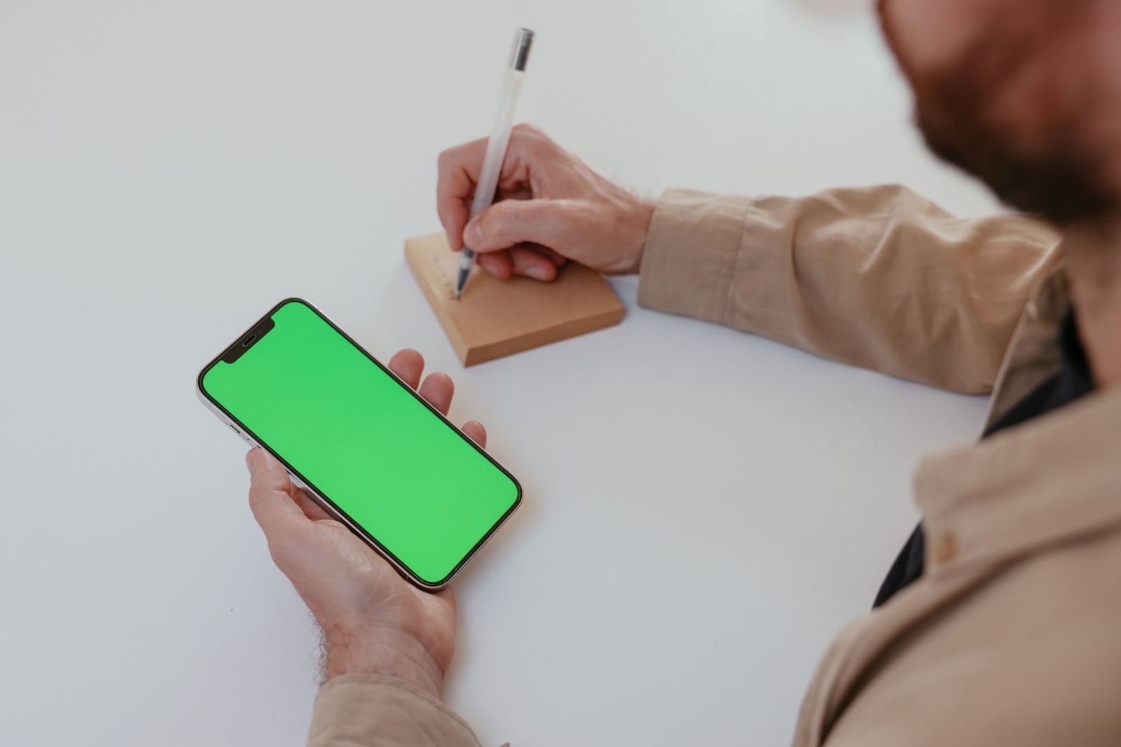 A person holds a smartphone and writes notes on a small notepad