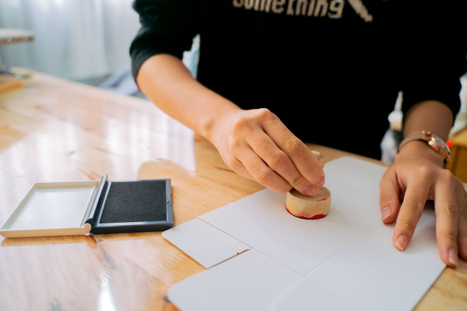 A person using a red ink stamp on a white piece of paper on a wooden table