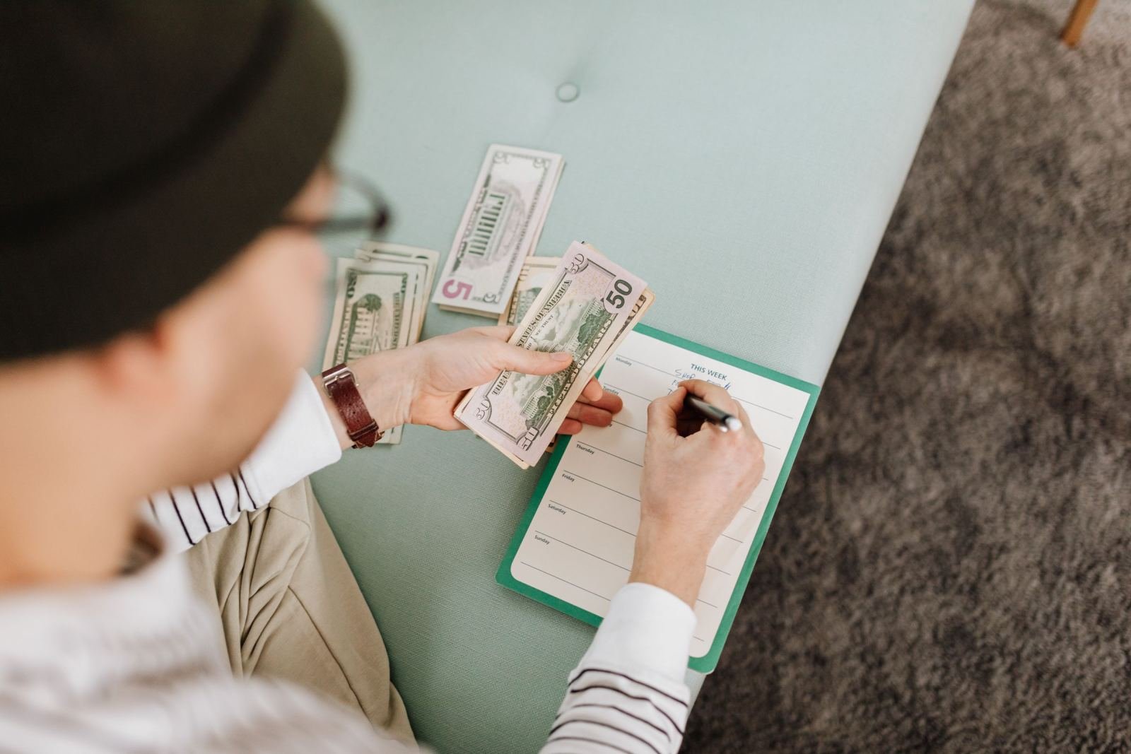 A person holding cash and writing on a weekly calendar at a table
