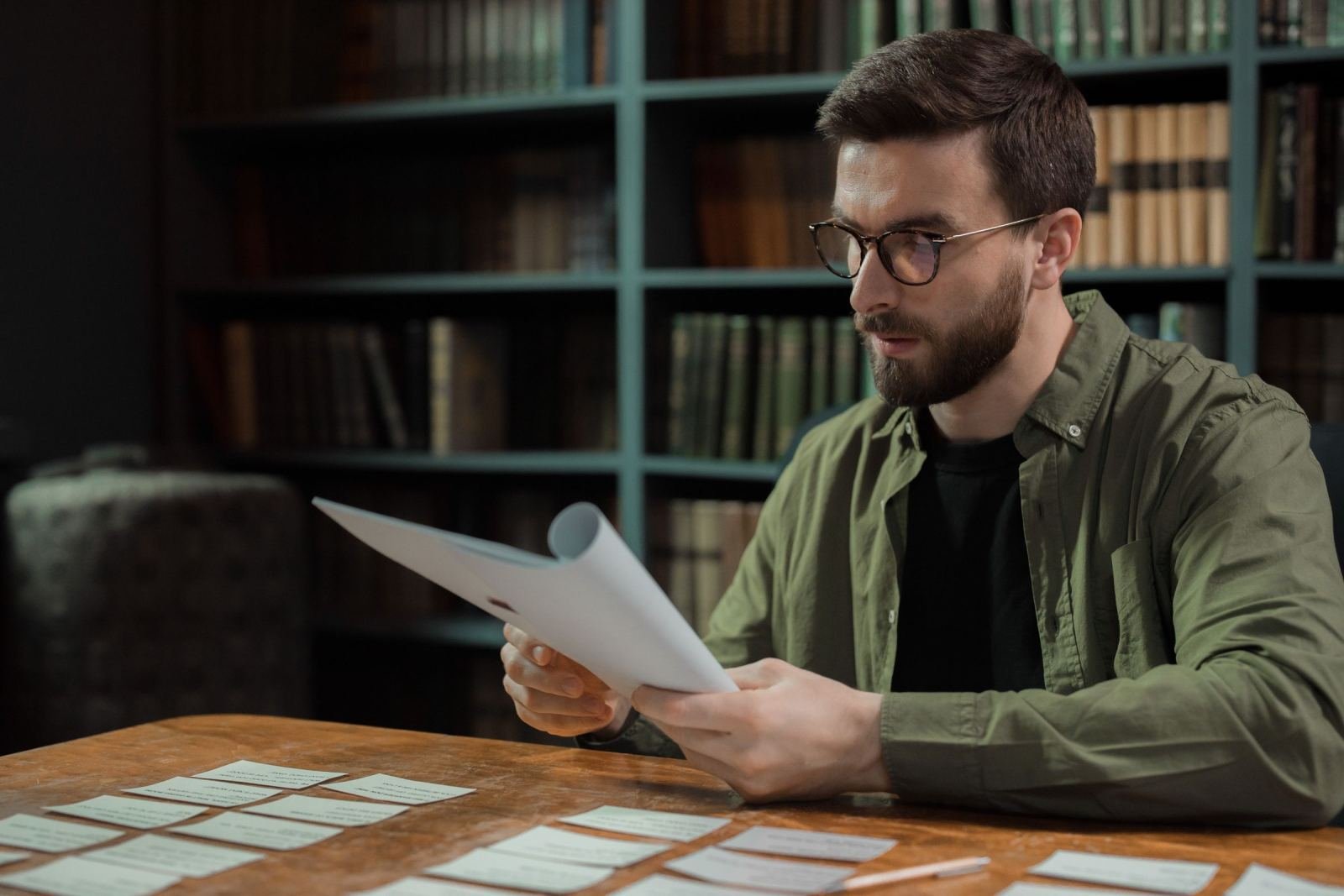 A man with glasses reads a document at a table with notes scattered in front of him