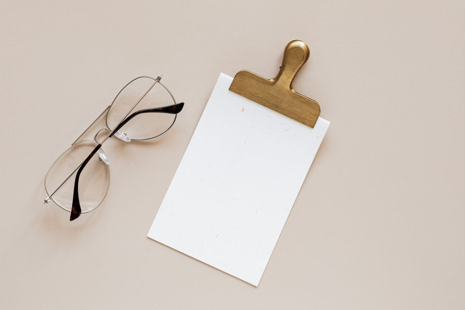 Round eyeglasses and a blank clipboard on a beige background