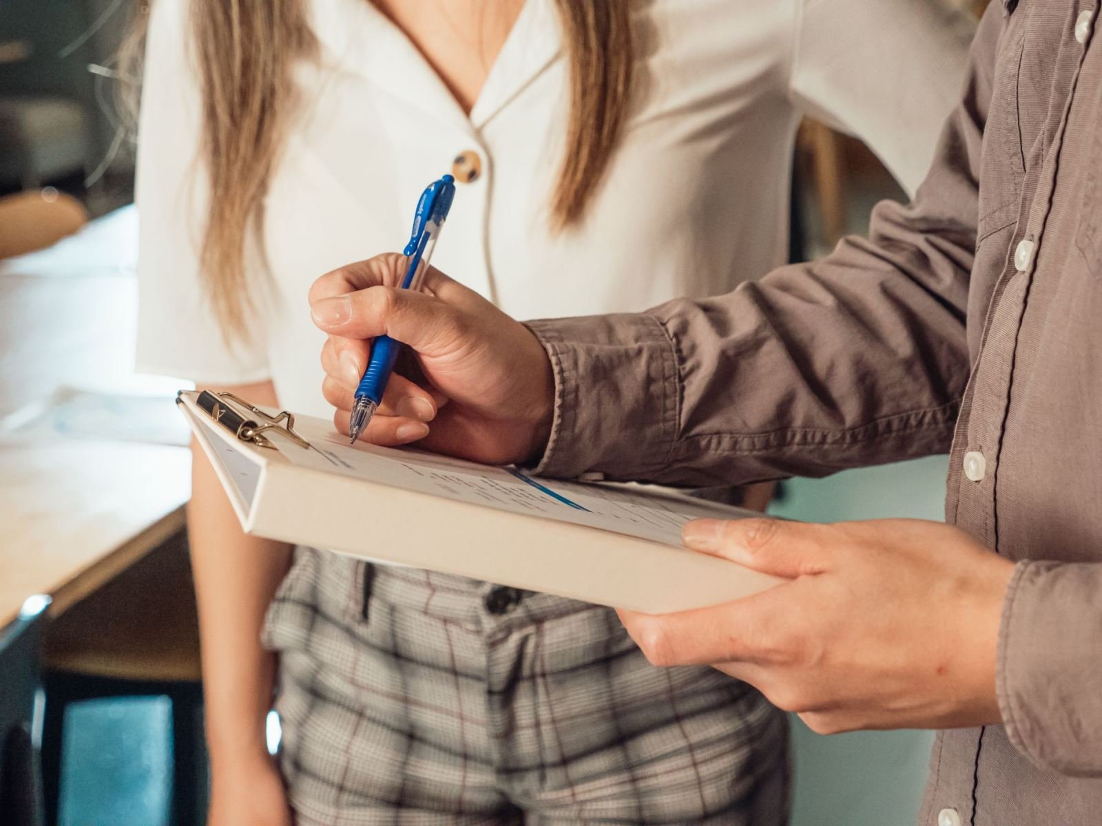 A person writing on a clipboard while standing next to another person