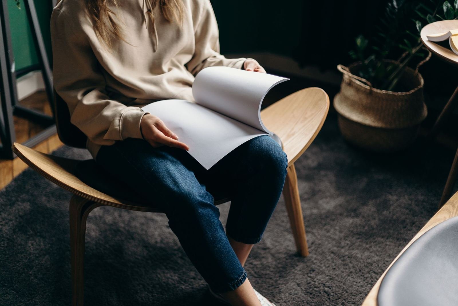 A person in a beige sweatshirt sits in a wooden chair reading a white booklet