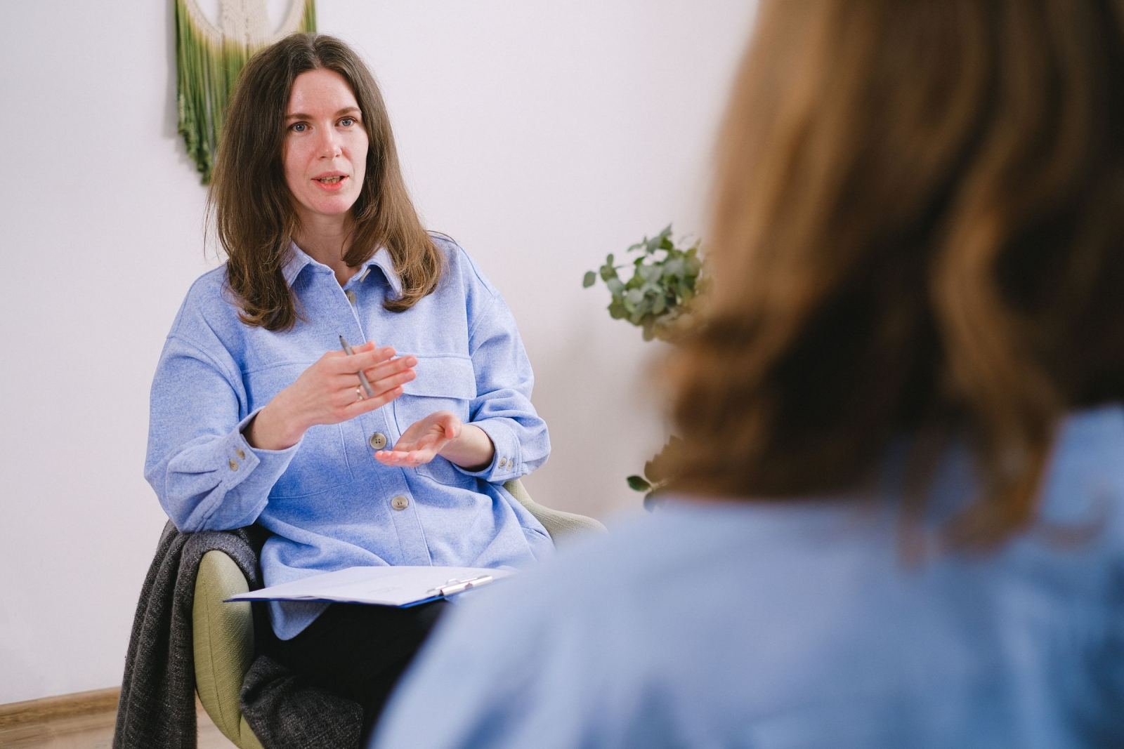 A woman in a blue shirt gestures while speaking to another person in an office