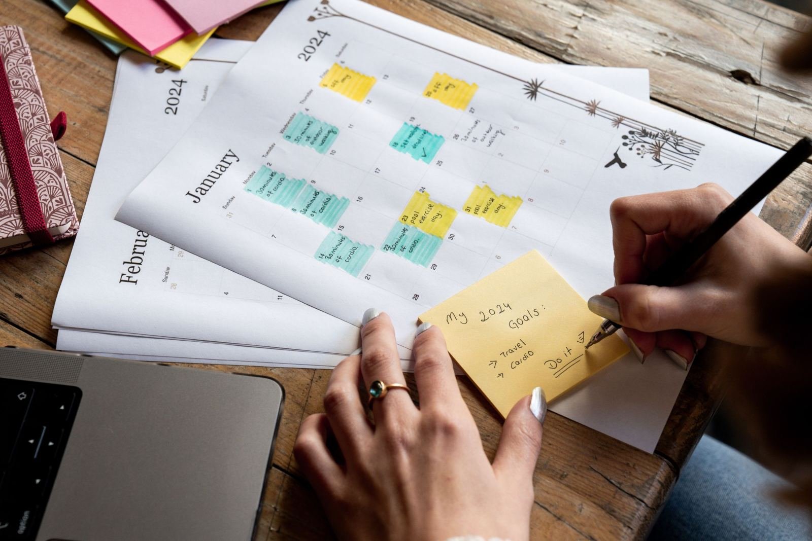 A person writes goals on a yellow sticky note over a 2024 calendar