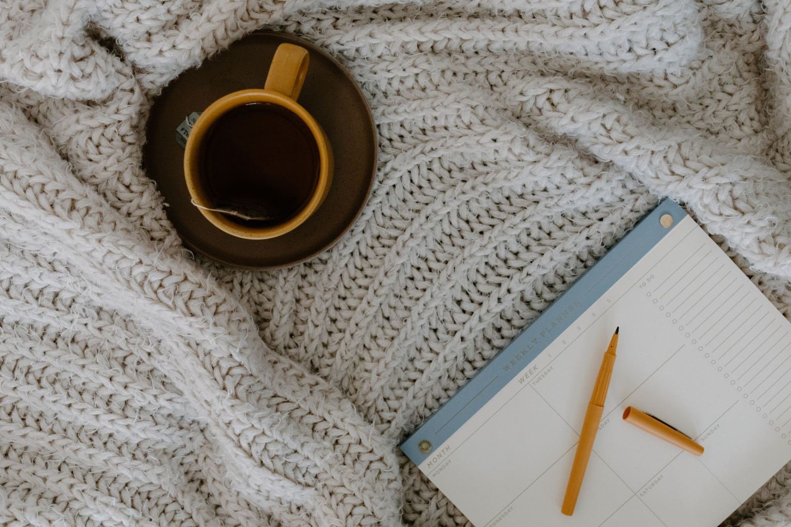 A yellow mug of tea and a weekly planner on a white knitted blanket