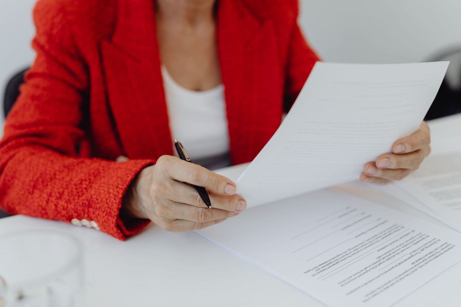 A person in a red blazer reviews a document with a pen in their hand