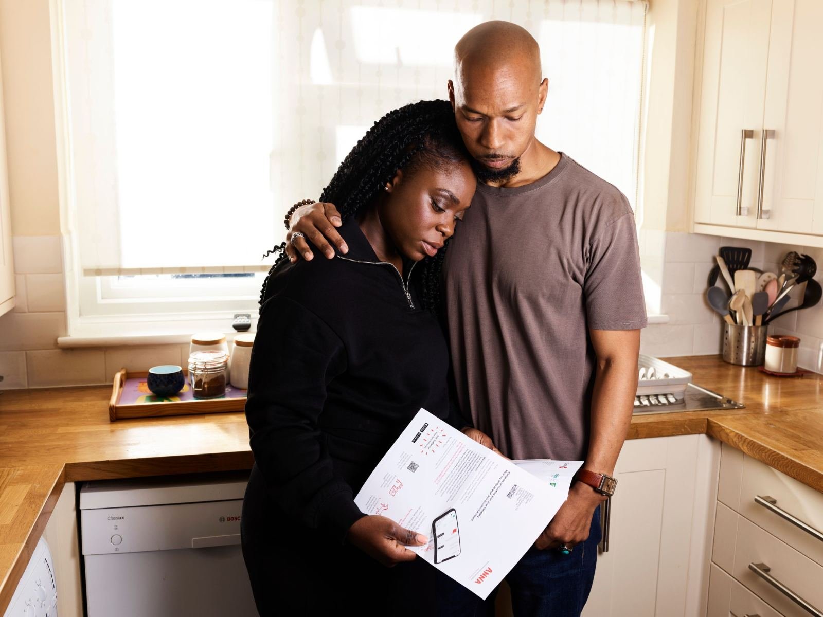 A man and woman look at a printed paper in their kitchen.