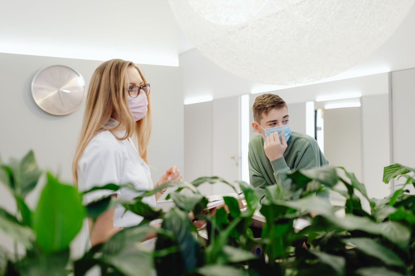 A medical professional in a mask speaks with a man in a mask in a bright office