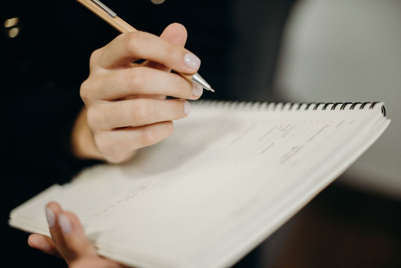 A close-up of a person writing in a spiral notebook with a pen