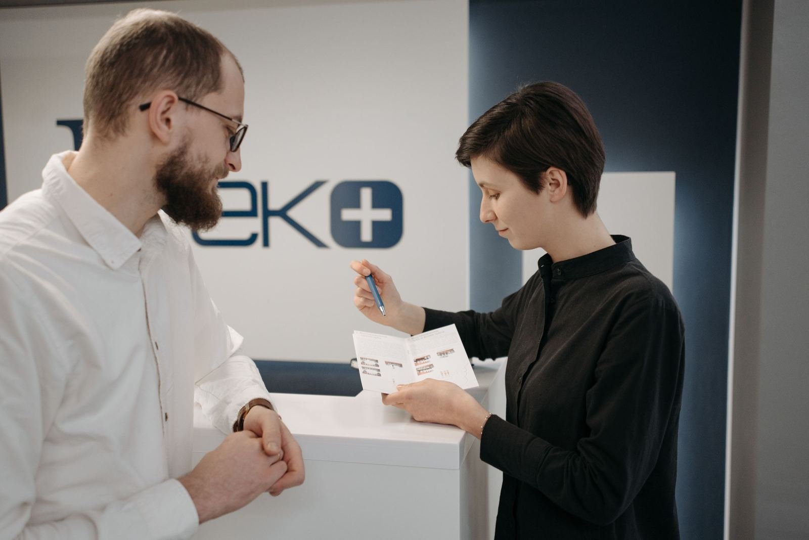 A staff member shows a brochure to a man at a white reception desk
