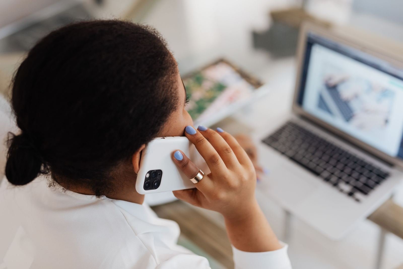 A woman on a phone call sits at a table with an open laptop