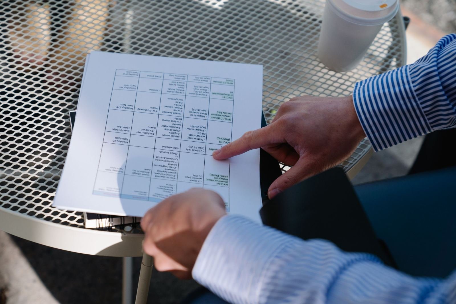 Someone wearing a striped shirt points at a chart on a paper document resting on a mesh table.