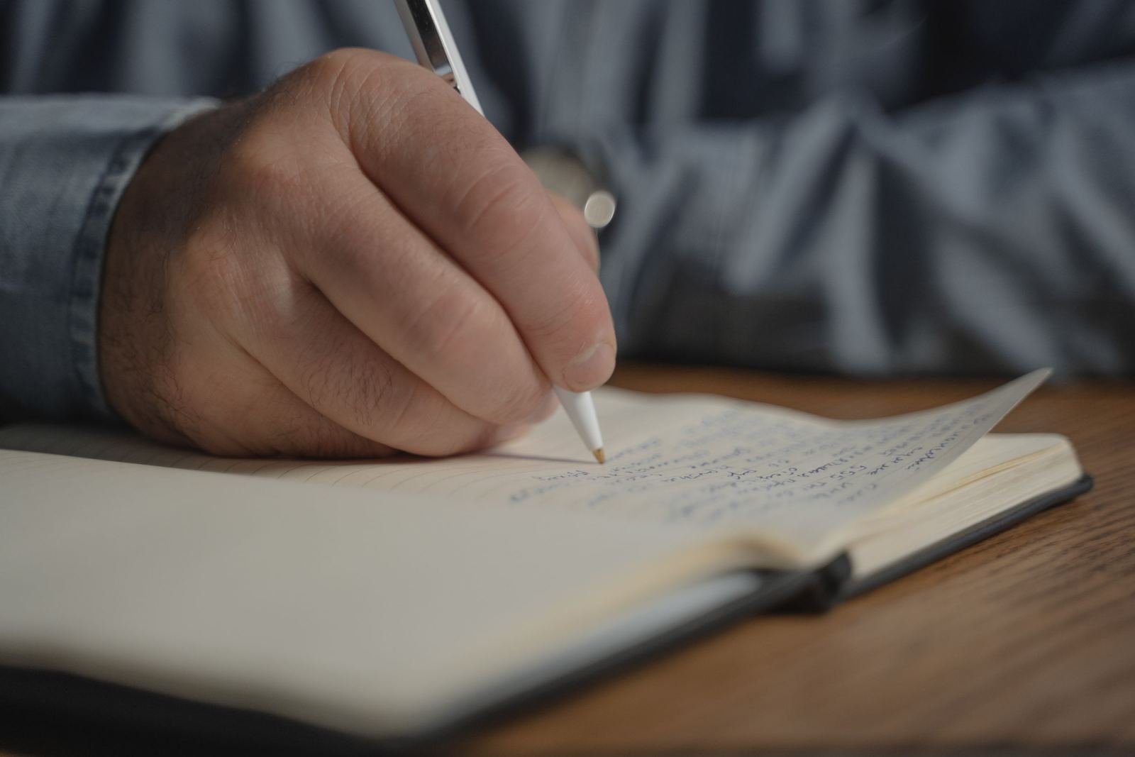A person's hand writing notes in a notebook with a pen