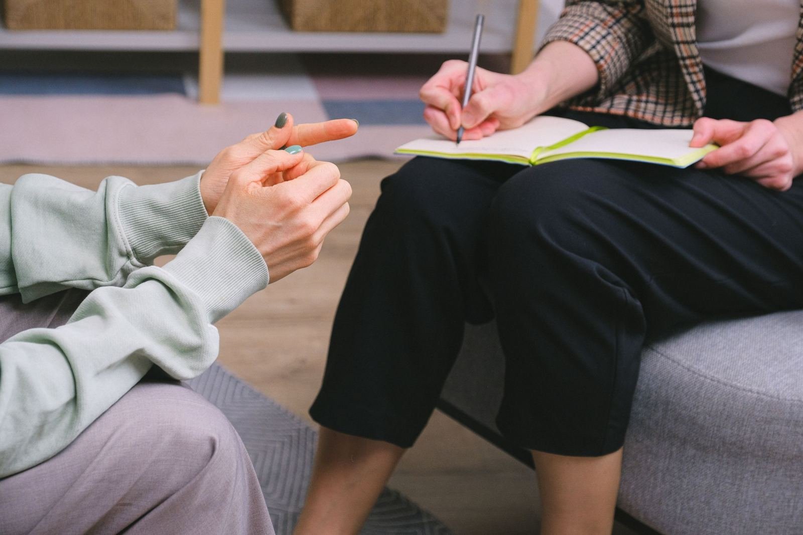 A person writing in a notebook while another person gestures during a conversation