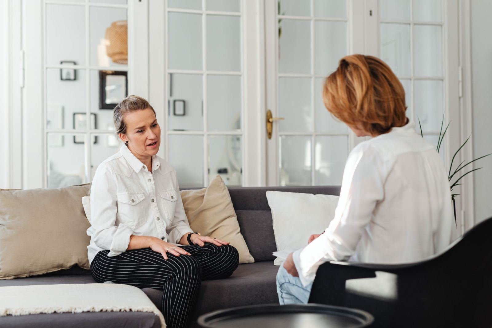Two women sit facing each other in a bright room during a conversation